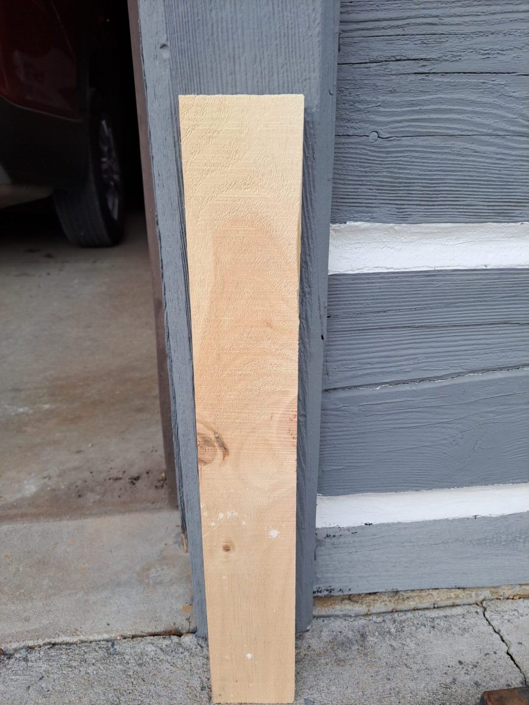 An outside of a door with a plank of wood kept outside with a gray color wall